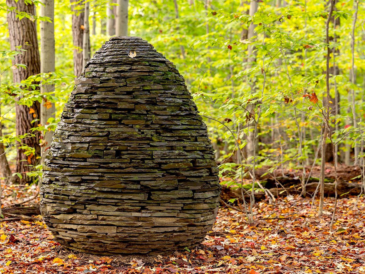 Egg-shaped sculpture of stacked stones in autumn woods.