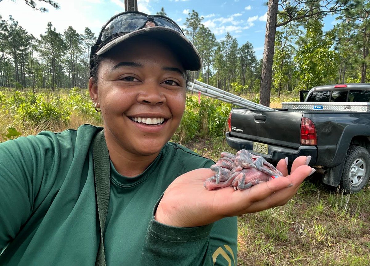 A smiling woman holds a handful of baby birds.