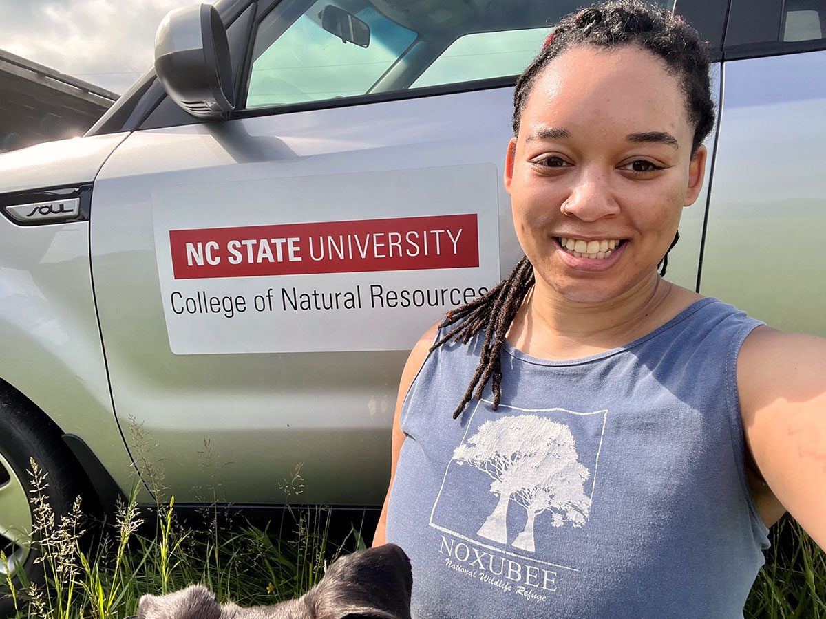 A smiling woman sits in front of a truck with a magnet: "NC State University: College of Natural Resources."