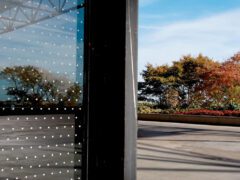 A corner of a building with white dots on its on its glass, showing how the dots break up the reflection.