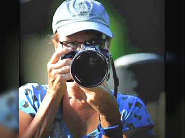 Woman with a baseball cap, looks into a camera with a large lens, looking at photographer..