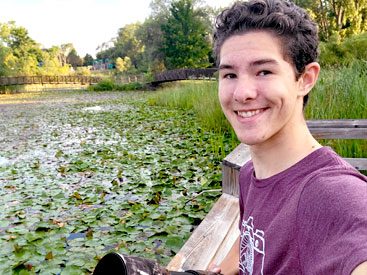 Young man smiling at the camera with lily-pad filled pond in background.