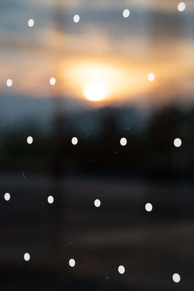 Dots on a window and burry reflection of sunset in the background.