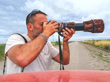 Man looking though a camera with a large lens.