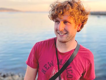 Young, smiling, man with red T-shirt and lake in background.