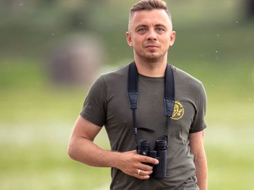 Short-haired man in khaki green T-shirt with binoculars.