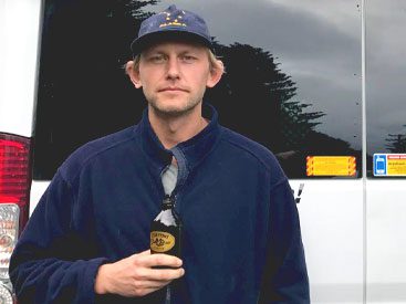 Man in a blue baseball camp and jacket stands in front of a van.