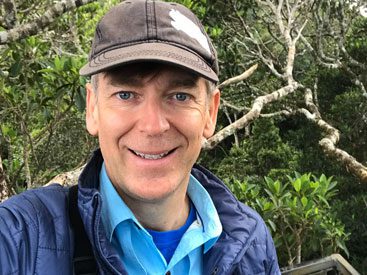 Smiling man with baseball cap and blue jacket.