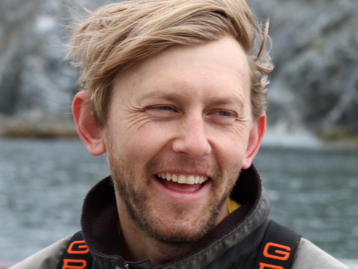 closeup of smiling man with gray water and rock in background